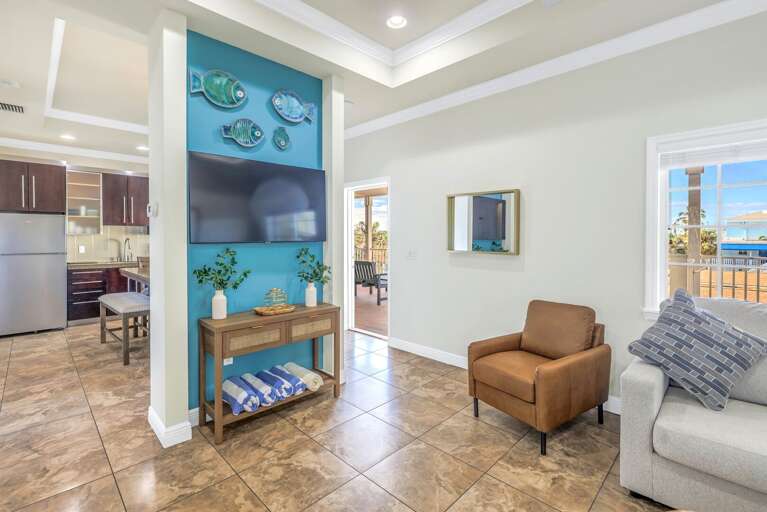 Spacious Living Area In Vacation Rental With Kitchen View, Bright Windows, And Beach-themed Decor