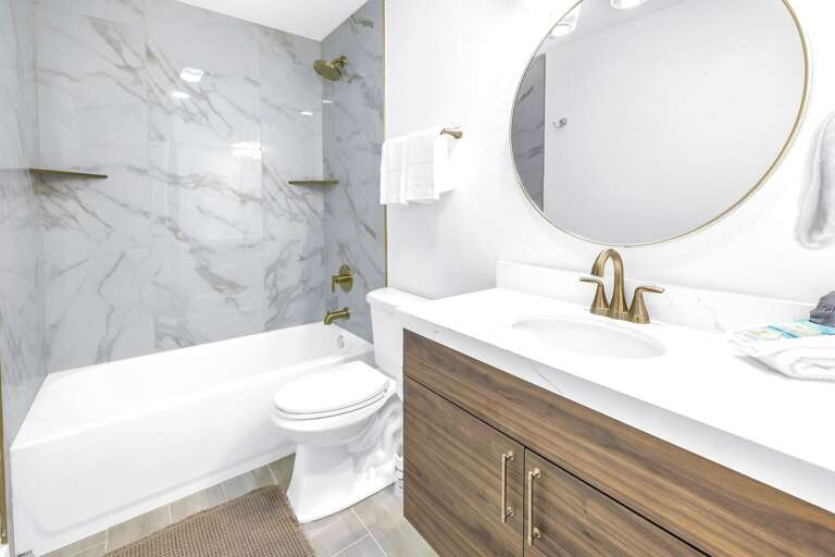 Bright bathroom with a marble-style tub/shower combination, modern vanity, and gold-accent fixtures.