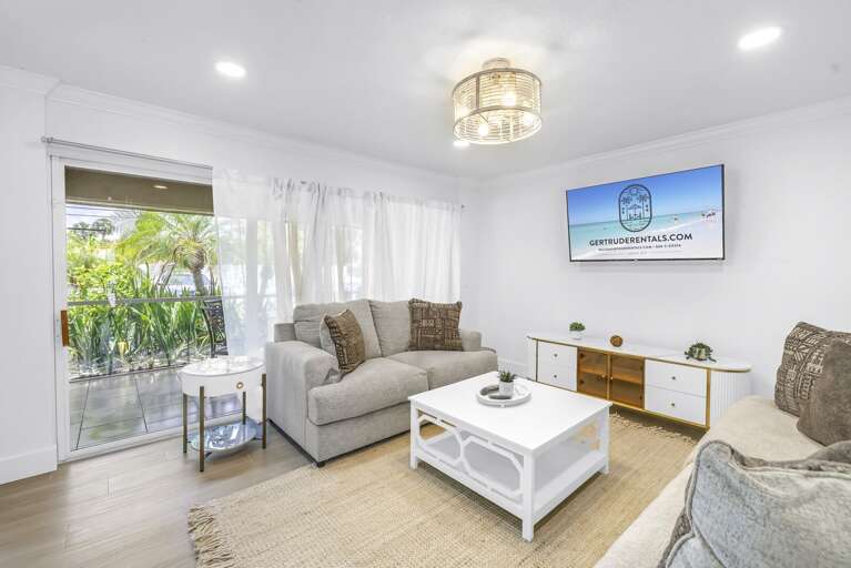 Comfortable living area with plush seating, flat-screen TV, and sliding glass doors to a lush garden view. Perfect for relaxing after a day at Siesta Key Beach.