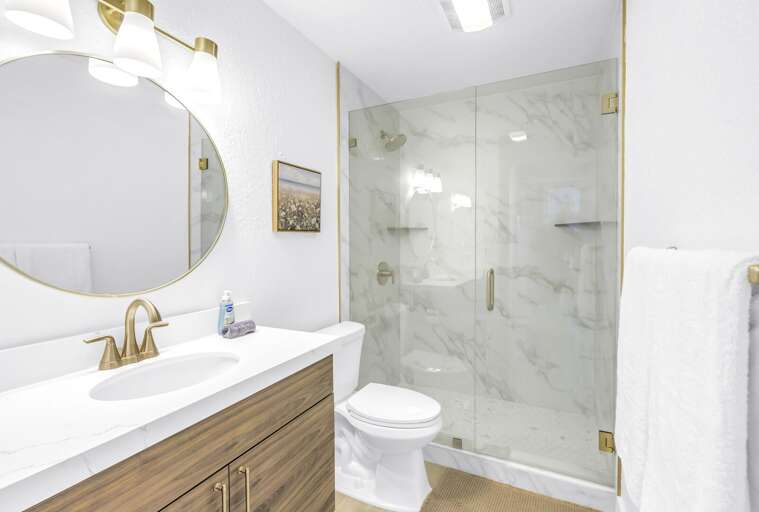 Elegant bathroom featuring a walk-in glass shower, marble-style tile, and a sleek vanity with gold fixtures.