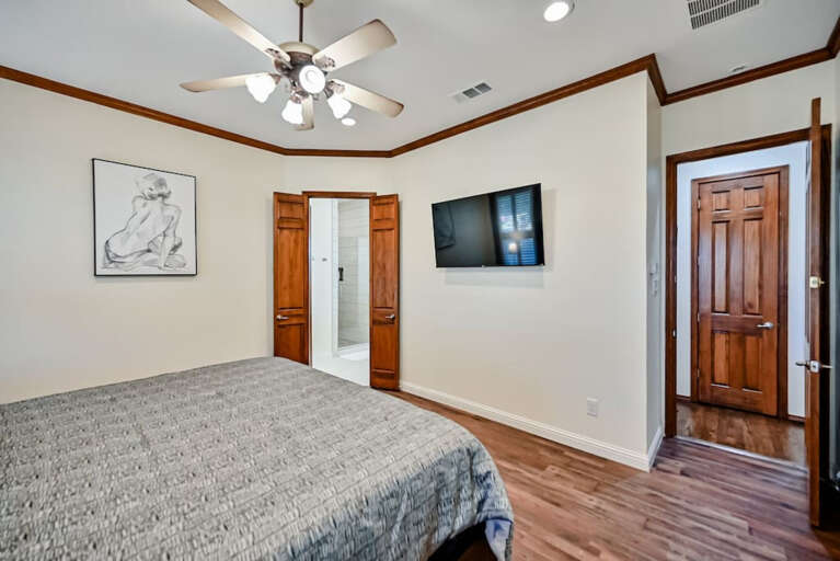 Inside master bedroom with TV across from California King bed, including view to entrance into master bathroom