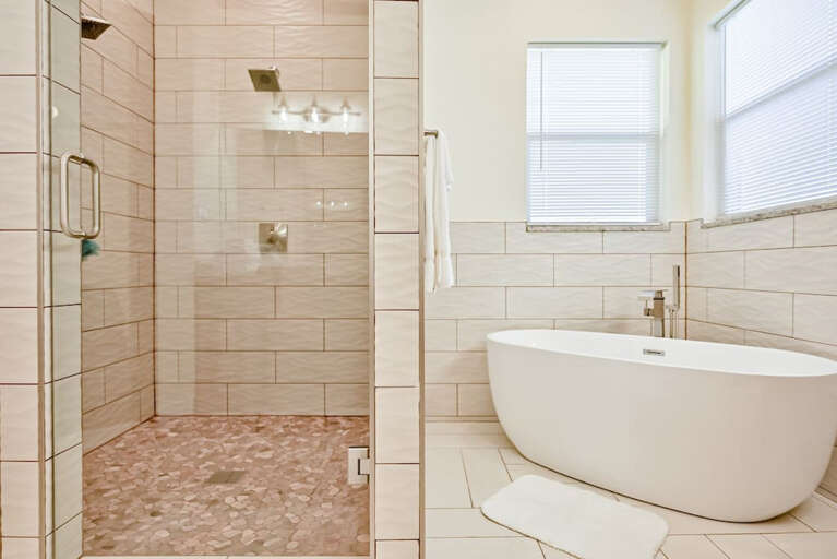 Large walk-in shower with two showerheads; bathtub separate from shower with solid wall between the two.
