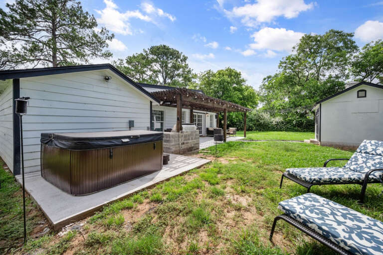 Hottub and lounging area in backyard with view of back patio on backside of house