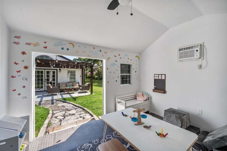 Children's Playroom with AC, various toys, and sitting area for children with adaptable chairs.  View back to walkway to back of house patio