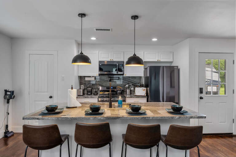 Bar seating area with 4 bar stools and full kitchen, view toward entryway and garage entry