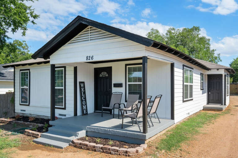 Front of property from front lawn looking down entry driveway, side entry door, into backyard, and front porch sitting area with 4 chairs for relaxing