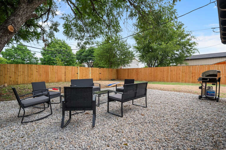 Backyard Outdoor Stone Gravel Sitting and Grill Area, with side yard dog run with new grass.  Cornhole boards and bags in throwing area in back.  Showing back gate that exits to alley way for back driveway exit.