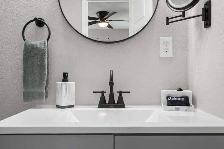 Primary En-Suite Bathroom with modern shower, vanity, toilet, lighted mounted makeup mirror for plenty of lighting, and walk in closet with hangers for clothing