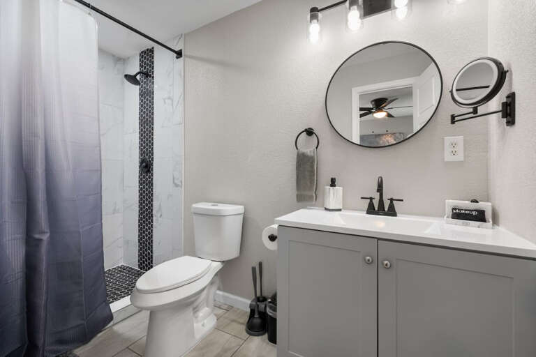 Primary En-Suite Bathroom with modern shower, vanity, toilet, lighted mounted makeup mirror for plenty of lighting, and walk in closet with hangers for clothing