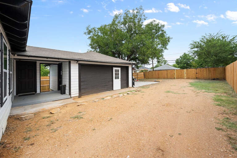Driveway and side entry view of back patio, garage, and view into dog run, and backyard exit gate to alley way