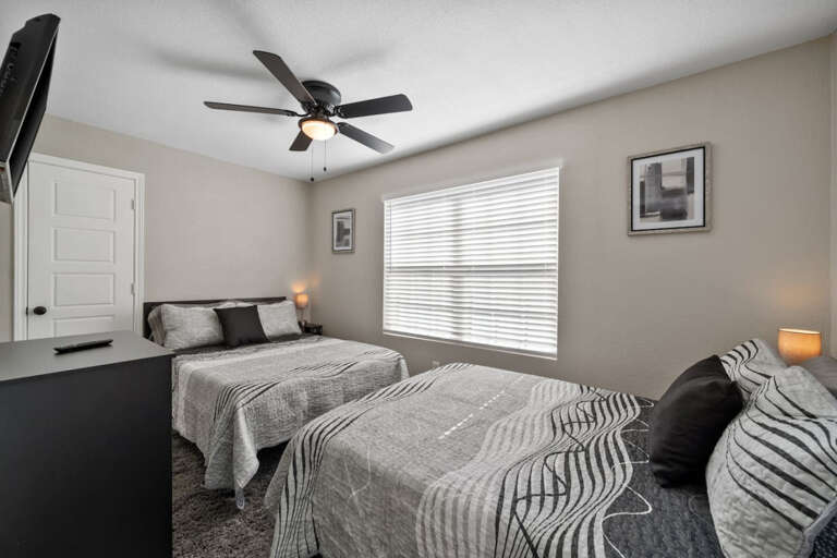 Third bedroom at front of house, with 2 Full-Sized beds, Smart Fire TV, ceiling fan, Dresser, nightstands with lamps and plugs, luggage rack, and closet with hangers