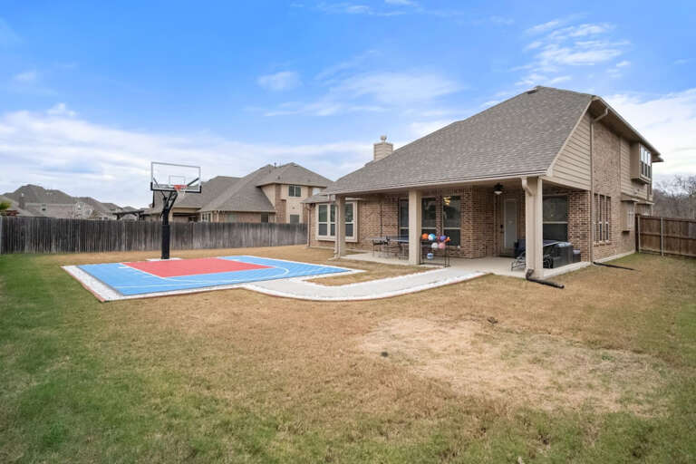 Full backyard view showing walkway to half court basketball court in backyard to enjoy with basketballs provided, as well as patio with ping pong and sitting area.