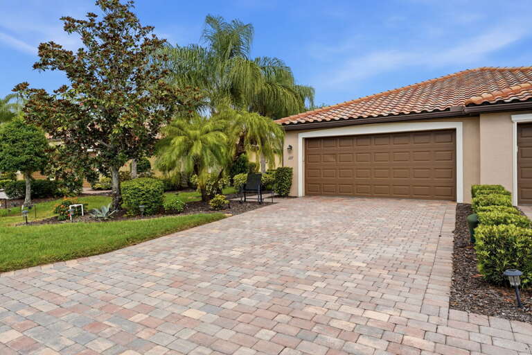 Welcome to 127 Babbling Brook Run — a tile-roof villa with a paver driveway and lush tropical landscaping on a quiet street in Riverstrand Golf & Country Club.
