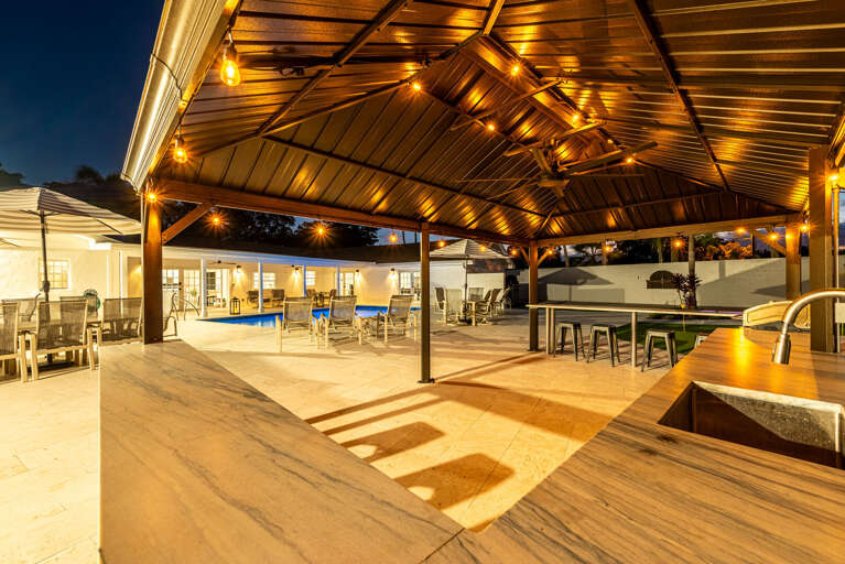 Your gazebo bar at night — string lights overhead, marble bar top, pool glowing in the background. Feels like your own private venue.