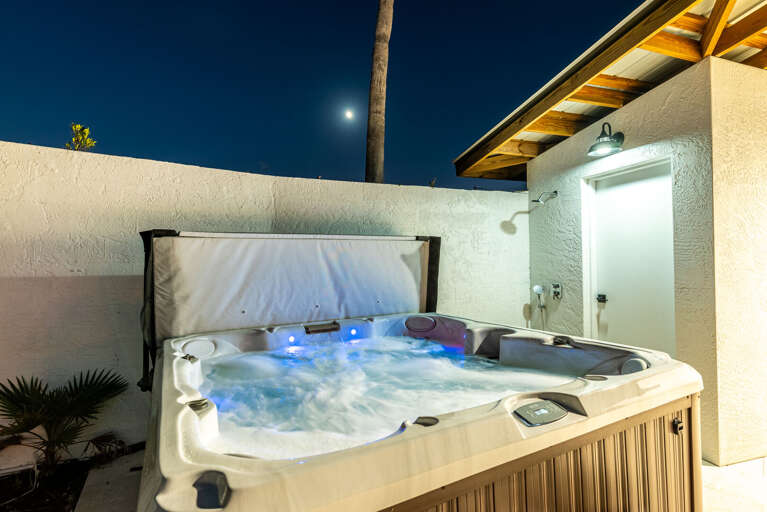 Your hot tub at night — blue LED lighting, moon overhead, outdoor shower steps away. The nighttime version of this patio is its own experience.