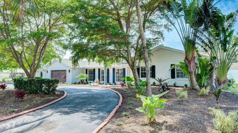 Your house from the front — circular driveway, mature shade trees, blue shutters. It doesn't look like a rental; it looks like the house your neighbors are jealous of.