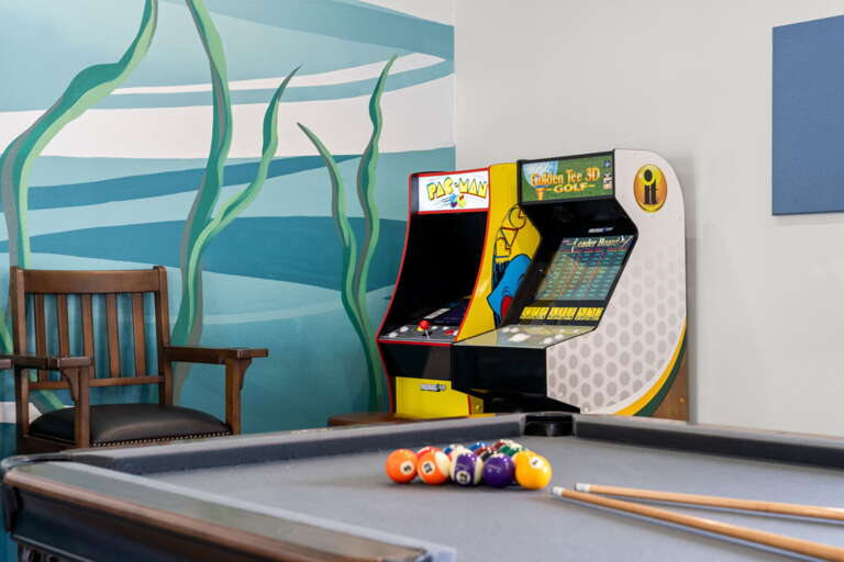 Pac-Man and a Golden Tee arcade machine against the underwater mural — your kids will lose track of time in here, and honestly so will you.