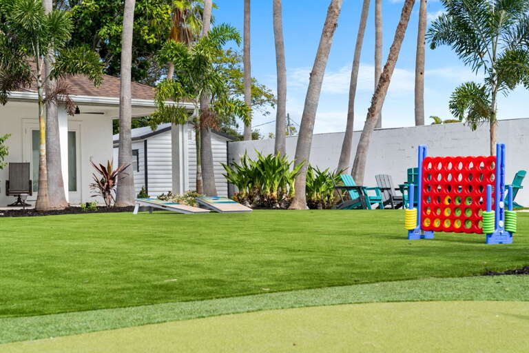 Your yard is always in session — Giant Connect Four on the turf, cornhole, and Adirondack chairs at the edges.