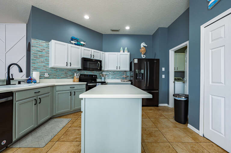 Cook like you mean it — the kitchen has a full island, teal tile backsplash, and black stainless everything