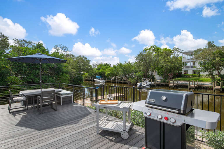 Fire up the Weber, set the cooler on the dock rail, and claim your table under the umbrella. The canal is right there — boats drifting past while you grill.