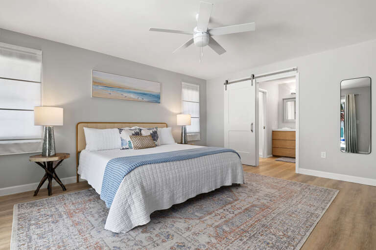 Your retreat at the end of a full day — a king bed, soft coastal light, and a private ensuite just through that barn door.