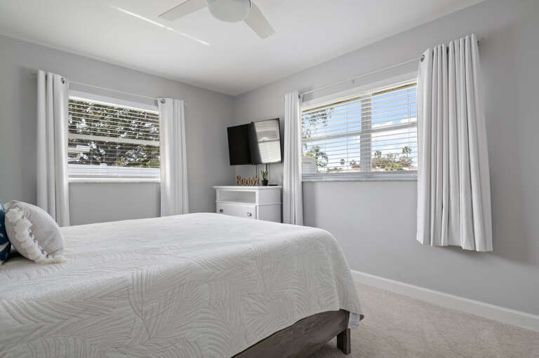 Sleep deeply in the queen room and let the morning light do the work — wall-mounted TV and two windows make it the quiet retreat of the house.