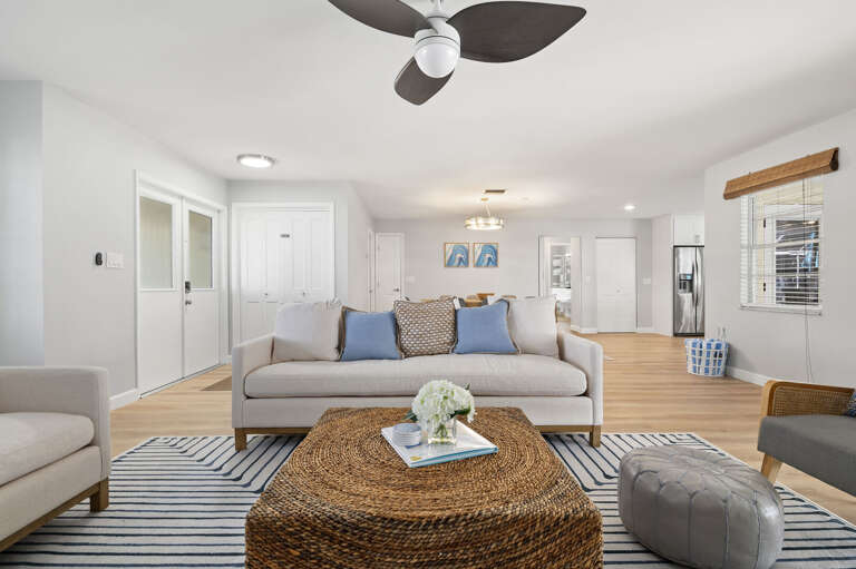 Spread out across the main living room — sofa space for everyone, ceiling fan overhead, pool view through the sliders.