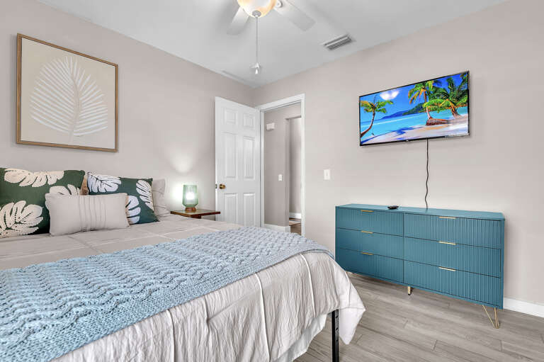 Claim the second queen room and you've got your own space — TV on the wall, tropical leaf art, completely separate from the main suite.