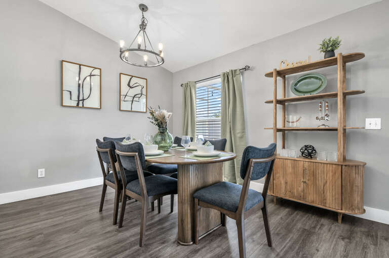 Gather everyone around the round pedestal table — six navy chairs, pendant chandelier, and enough room that elbows stay on the table.