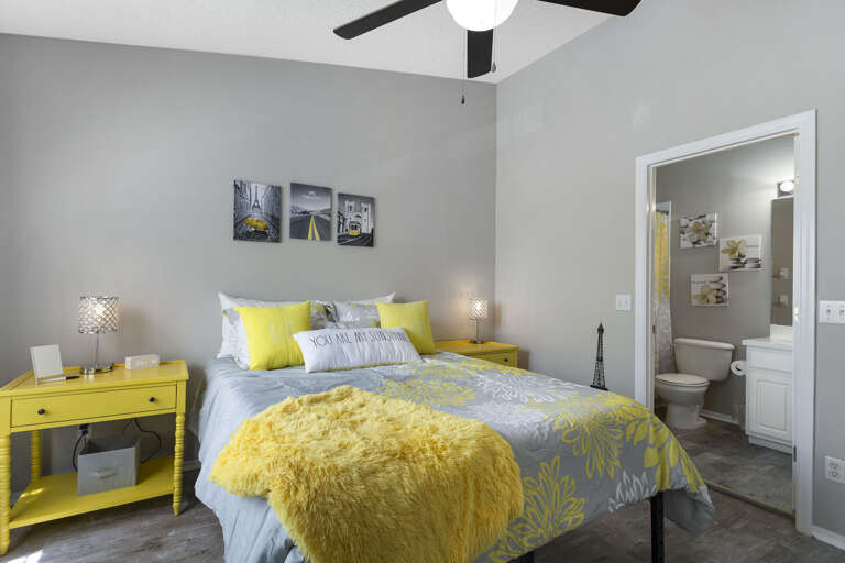 Your primary suite with yellow bedding and a ceiling fan — a quiet, private space that's all yours.