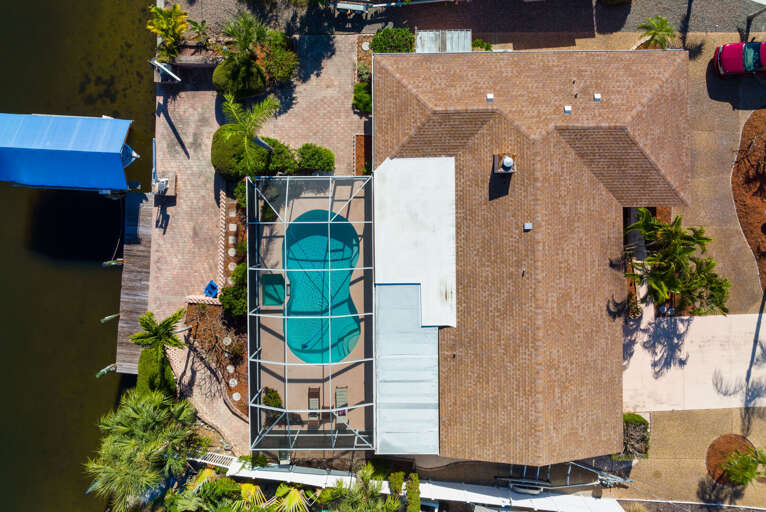 Take in your full footprint from directly above — screened pool enclosure, boat dock, and tropical landscaping all in one shot.