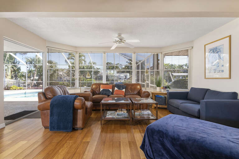 Gather everyone on the leather sectional and let the wall of windows do the talking — your pool shimmers just beyond the glass, blurring the line between inside and out.