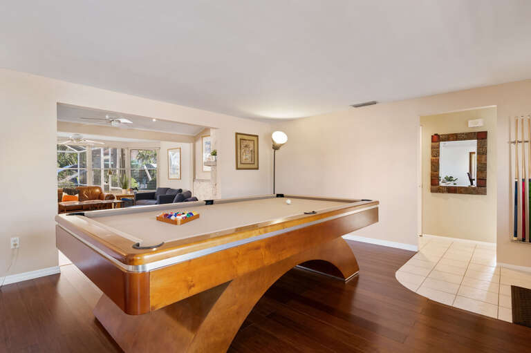 Play from any angle — the billiards room is wide enough for a full backswing on every side, with the cue rack on the wall and hardwood floors underfoot.