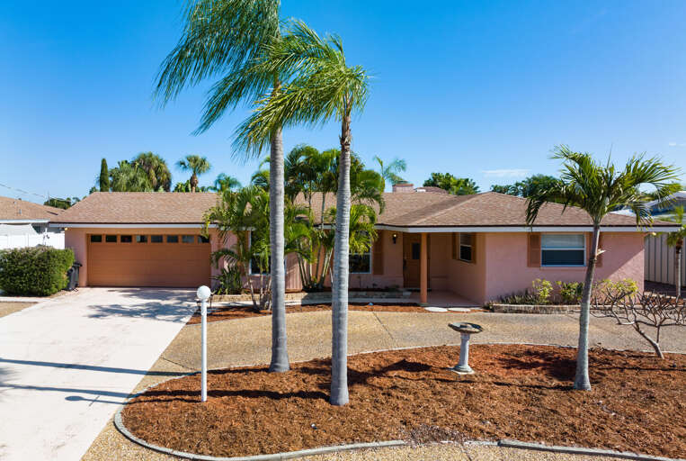 Pull into the wide driveway and you're greeted by a well-manicured single-story home framed by palm trees — plenty of space to park and unload before you head straight to the pool.