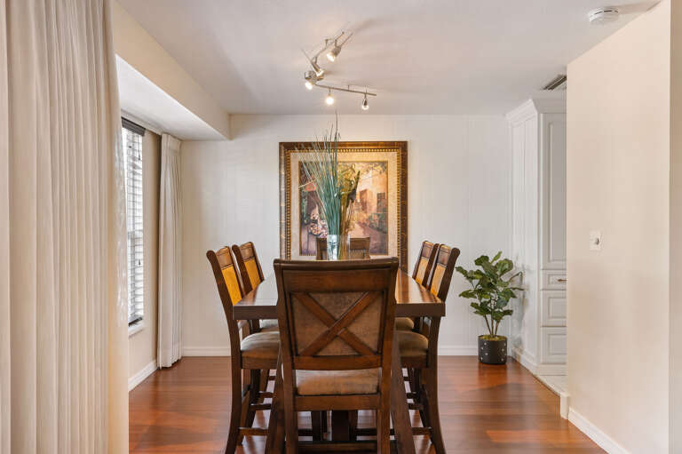 Seat all four guests at the solid six-chair dining table — track lighting overhead, hardwood floors underfoot, and large framed artwork giving the room a polished, finished feel.