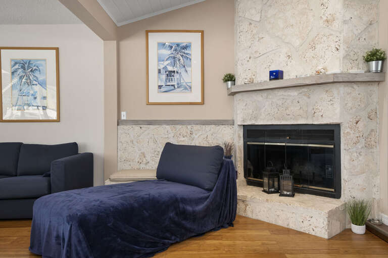 Sink into the navy chaise beside a crackling fire — the stone fireplace with coastal lanterns on the hearth is the kind of cozy corner that makes a cold evening feel like a reward.
