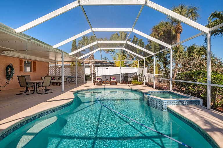 Step through the screen door and you're immediately poolside — the full enclosure, pool, and surrounding tropical greenery make this backyard feel like your own private resort.