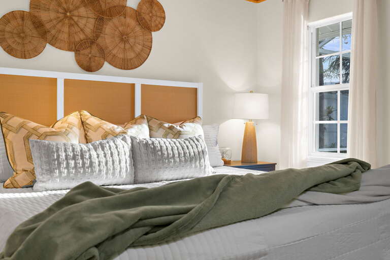 Feel how the layered pillows and orange headboard pull together the whole coastal palette — the woven wall piece above the bed is the kind of detail guests always photograph before they check out.