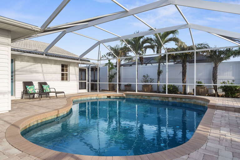 Float in the kidney-shaped pool while the palms sway above the screen — the enclosure keeps it breezy and private, and the paver deck gives you room to spread out however you like.
