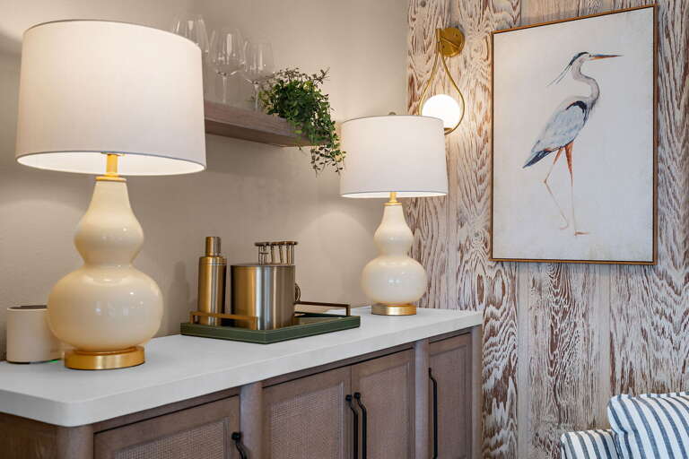 Notice the thought in the decor details — ceramic gourd lamps, brass accents, and heron art that connects the indoor palette directly to the waterfront outside the windows.