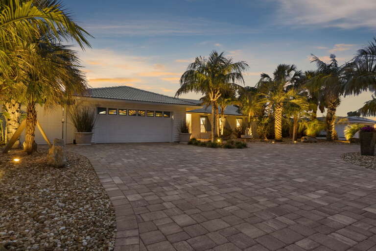 Pull into the wide paver driveway and feel the vacation officially begin — uplighted palms, warm window glow, and a front facade that photographs exactly as well as it looks in person.