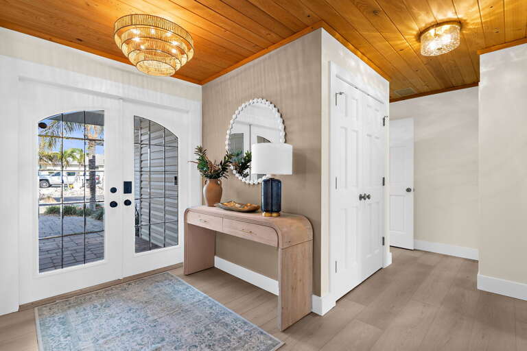 Your first look inside sets the tone for the week — the chandelier warms the entryway, the wood ceiling runs the length of the hall, and the whole house opens up invitingly in front of you.