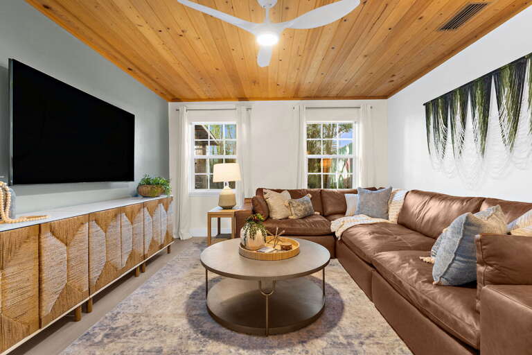 Sink into the oversize leather sectional after a full day on the water — the wood-plank ceiling, the smart TV, and the coastal light through the windows make staying in feel like a reward.