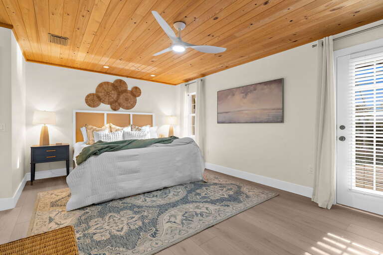 Sleep past sunrise in the primary king — the French doors face out to the yard and the wood-plank ceiling keeps everything quiet, cool, and genuinely restful through the whole night.