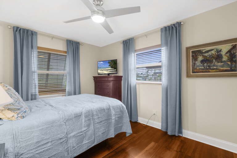 Your second guest room is dressed and ready — queen bed, ceiling fan, dresser with TV, and enough space for a full week of beach gear.