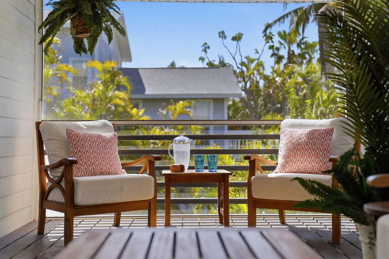 Claim the balcony armchairs for the morning — teak seating, patterned pillows, and tropical treetop views from the second floor.