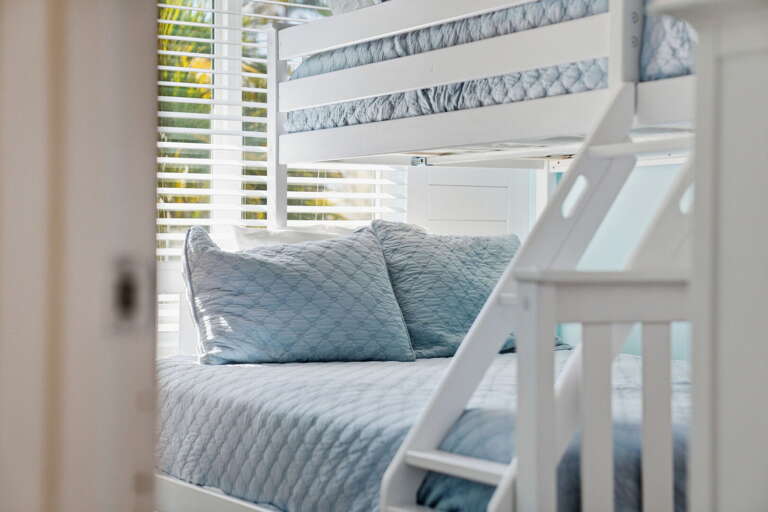 Claim the lower bunk — blue quilted bedding, your own ladder, and plantation shutters keeping the morning light gentle.