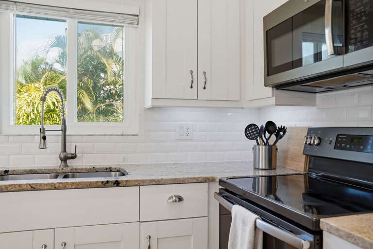 Cook the big dinner on the stainless electric range — microwave above, white cabinets on every side, and a breeze through the window.