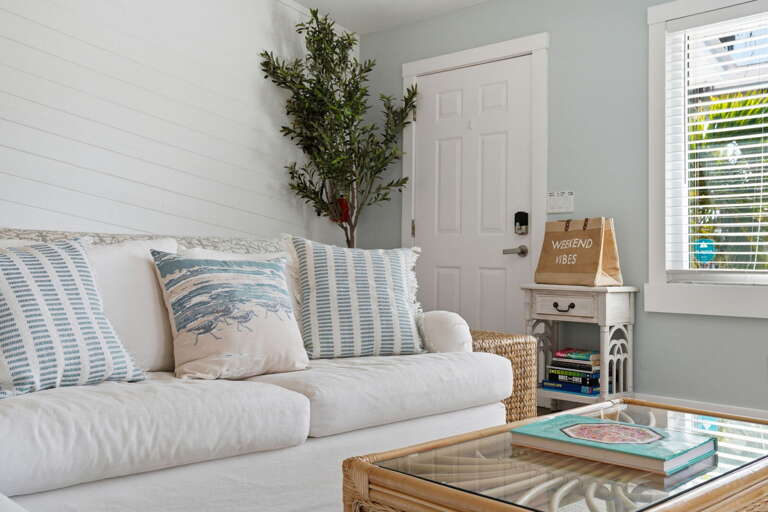 Drop your beach bag and sink into the sofa corner — coastal throw pillows, wicker side table, and the front door right behind you.