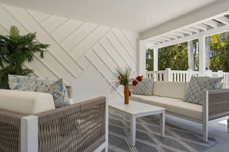 Find your spot on the covered porch — two white wicker sofas, a coffee table, and tropical garden views to melt into.